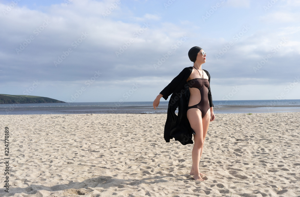 woman standing on the beach with a swimming costume on and 1950's swim hat and sunglasses woman standing on the beach with a swimming costume on and 1950's swim hat and sunglasses