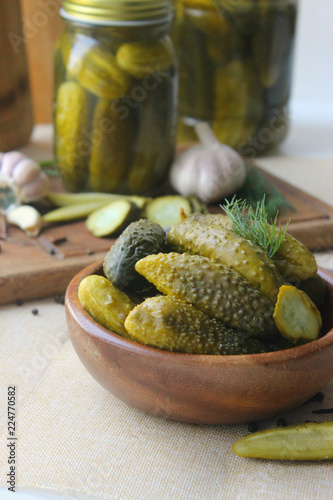 Cucumbers in a wooden bowl, fresh herbs, pickling spices and jars of pickled cucumbers on the table