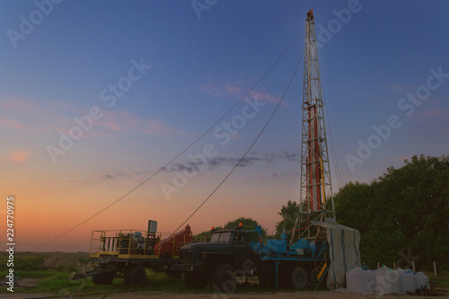 drilling rig drills a well for the extraction of drinking water at sunset under a beautiful sky for drinking people photo