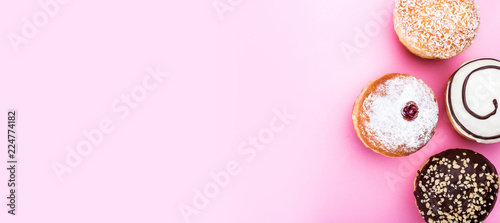 Sweet and fresh doughnuts with chocolate cream, coconut and sugar powder isolated on pink background, top view and copy space