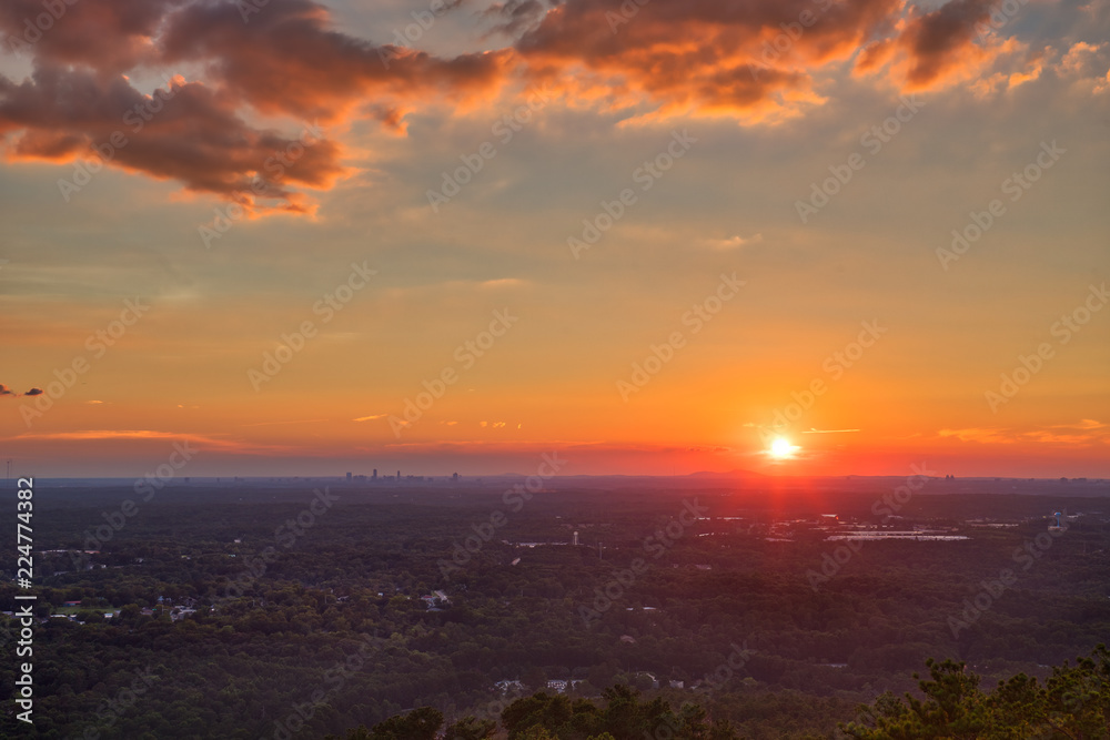 Beautiful orange, red, pink, yellow sunset with clouds and a blue sky looking out over the trees towards Atlanta, GA from Stone Mountain