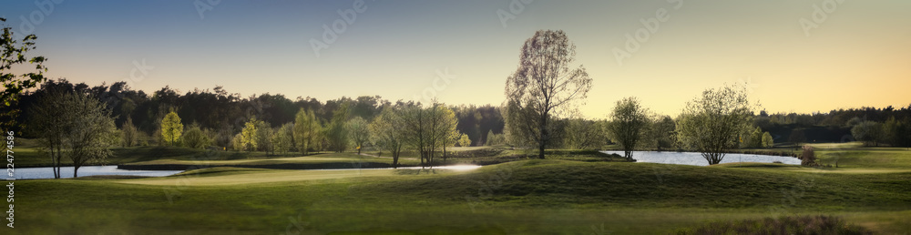 Panorama von einem Golfplatz mit Bäumen Büschen und Teichen im Sonnenuntergang