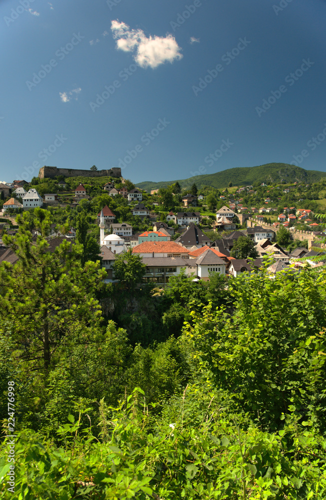 Obraz premium Overlooking city of Jajce from a nearby hill. A magnificent fortress is placed at the tom of a hill in the middle of the city, below are mosques and churches.
