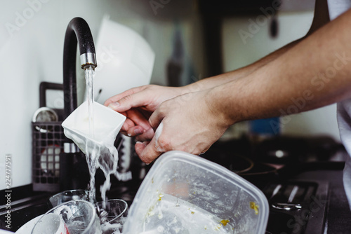 The man cleans the cup after coffee with a scourer. Dirty dishes in the sink. No dishwasher. Concept of caring for dishes in the kitchen. The kitchen sink is full of dirty dishes.