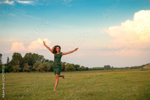 Beautiful young woman running on a meadow at sunset