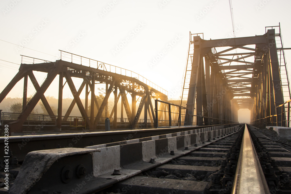 A railway bridge in the morning fog or smoke through which the rays of the sun shine