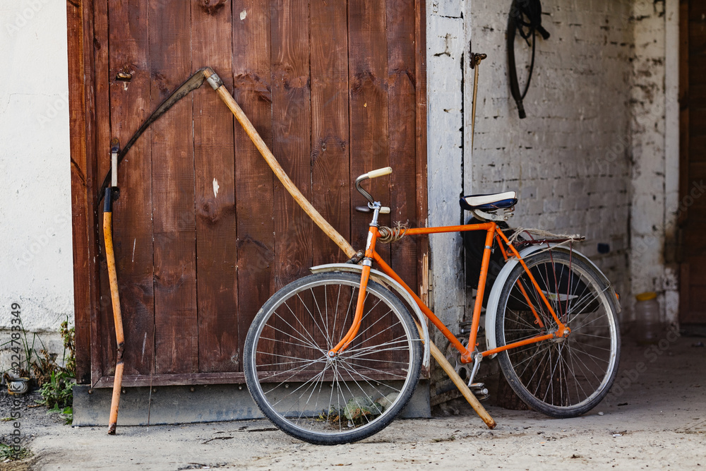 retro bicycle and scythe stand at the wall of a farmhouse retro bicycle and scythe stand at the wall of a farmhouse