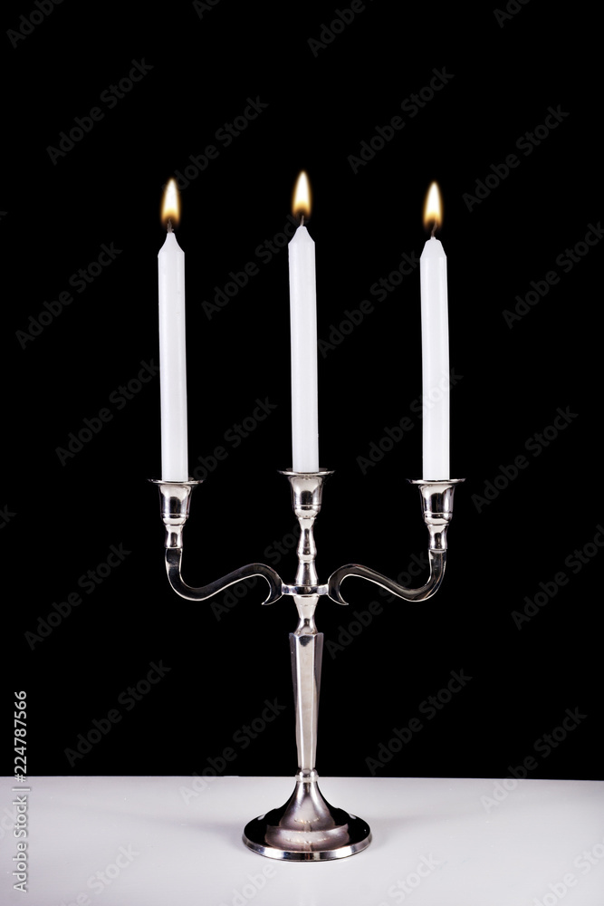 Silver baroque candlestick with three white paraffin candle burning on desk and black background. Romantic and stylish concept.