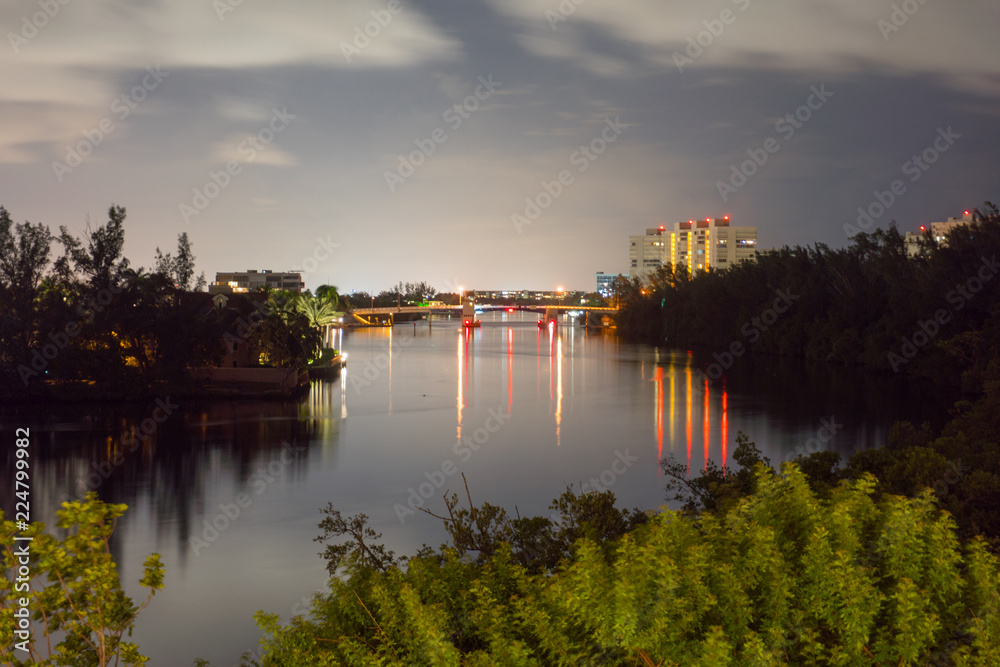 Night time long exposure photo overlooking river and city in background. Skyline light illuminate water and drawbridge under evening clouds
