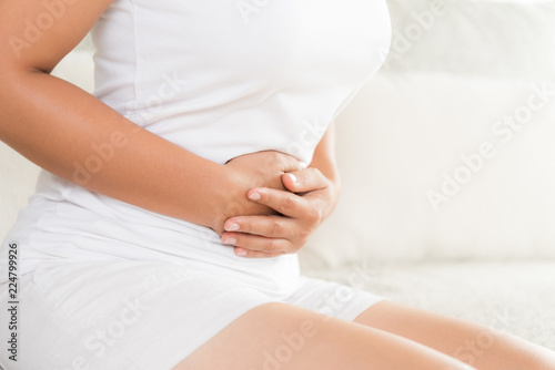 Young woman having painful stomachache sitting on sofa at home. Chronic gastritis. Abdomen bloating concept.