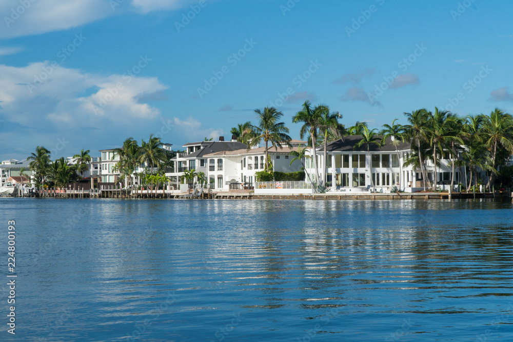 Day time exterior wide establishing shot of luxury mansion homes along inner coastal waterway river in Florida. Tropical vacation and summer home destination upper class living