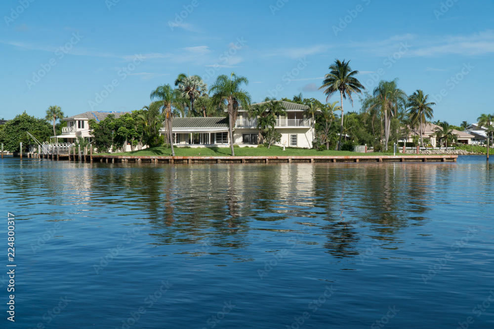 Day time exterior establishing shot of generic mansion along river in tropical island location. Palm trees and calm water in backyard of luxury home in beautiful summer destination