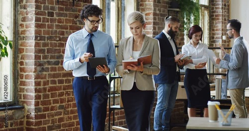 Caucasian attractive man and woman standing in the loft conference hall and discussing some issues of the company with tablet device and notebok in hands. photo