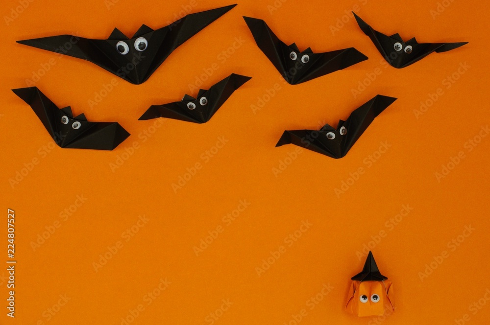 The origami Halloween background of pumpkin head jack-o-lantern looking up at the flying bats isolated on orange background with space for text.