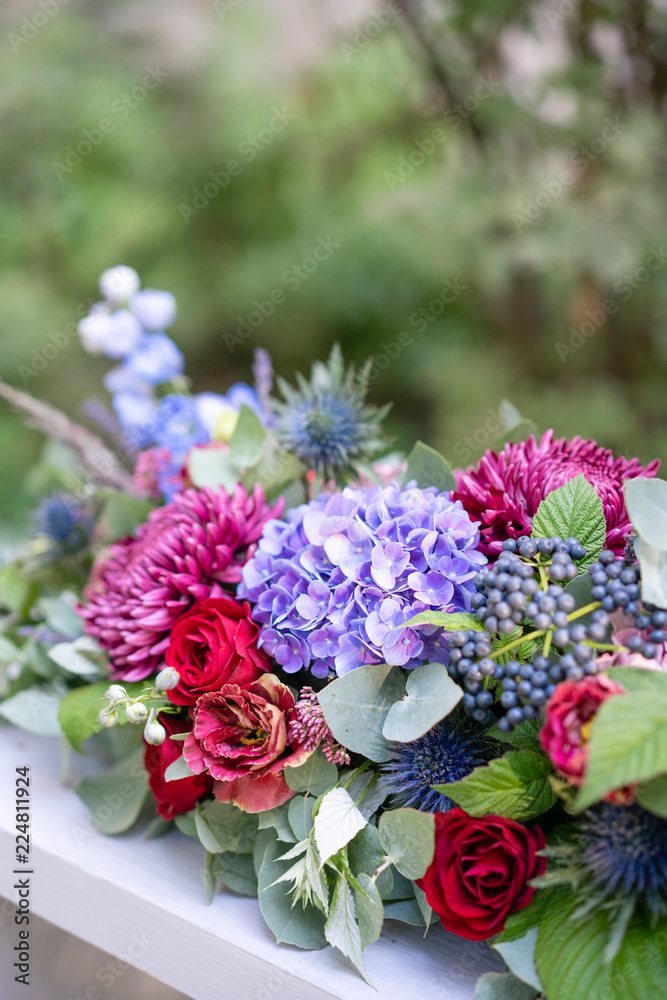 Elongated floral arrangement in vintage metal vase. table setting. Blue and red color. Gorgeous bouquet of different flowers. Park on background