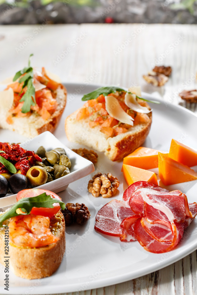 Plate with Italian appetizers. Bruschetta with a cherry tomatoes and shrimps. Parmesan cheese, prosciutto, green capers, olives, sun-dried tomatoes and walnuts. Plate with Italian appetizers. Bruschetta with a cherry tomatoes and shrimps. Parmesan cheese, prosciutto, green capers, olives, sun-dried tomatoes and walnuts.