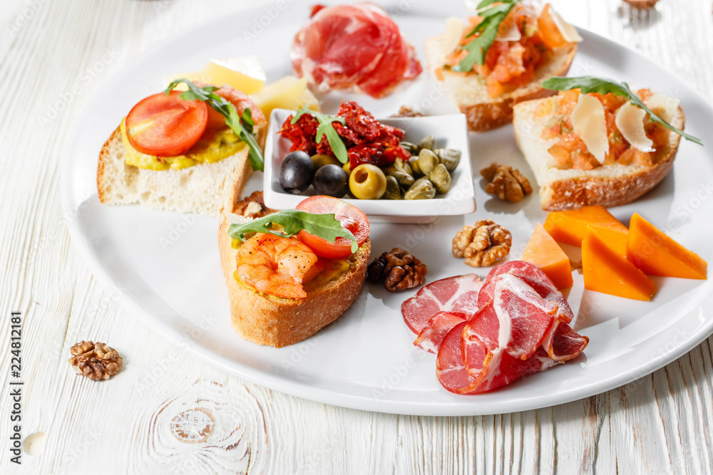 Plate with Italian appetizers. Bruschetta with a cherry tomatoes and shrimps. Parmesan cheese, prosciutto, green capers, olives, sun-dried tomatoes and walnuts.