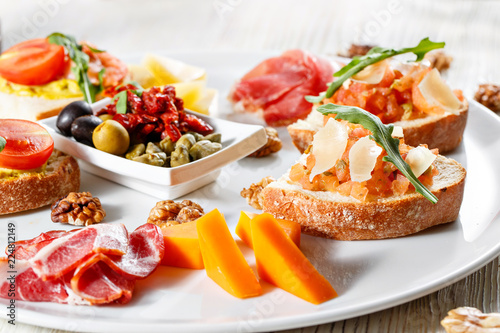 Plate with Italian appetizers. Bruschetta with a cherry tomatoes and shrimps. Parmesan cheese, prosciutto, green capers, olives, sun-dried tomatoes and walnuts.
