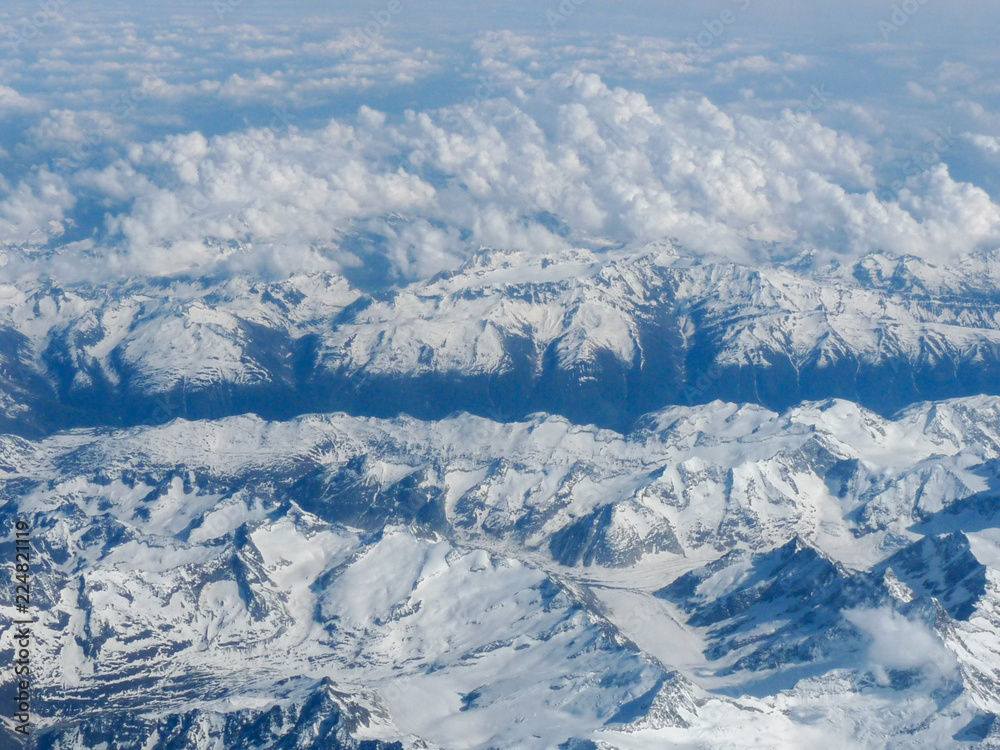 view of the snow-covered peaks of the mountains hidden behind the clouds from the window of the plane