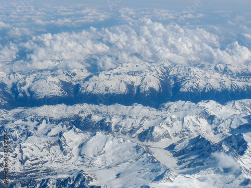 view of the snow-covered peaks of the mountains hidden behind the clouds from the window of the plane