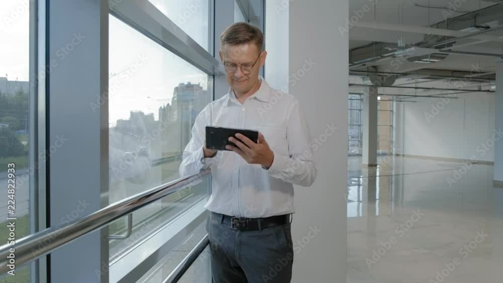 Mature businessman at a window with a tablet Mature businessman at a window with a tablet