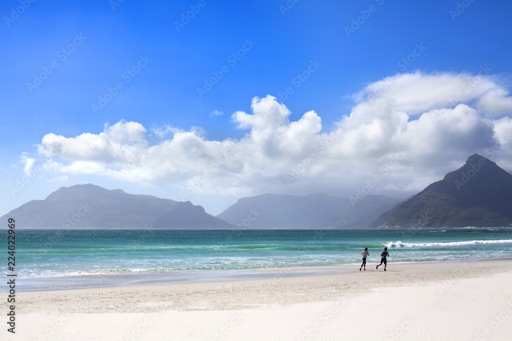 Girl and boy running on white sand beach, blue sea, waves, sky and mountains with clouds background