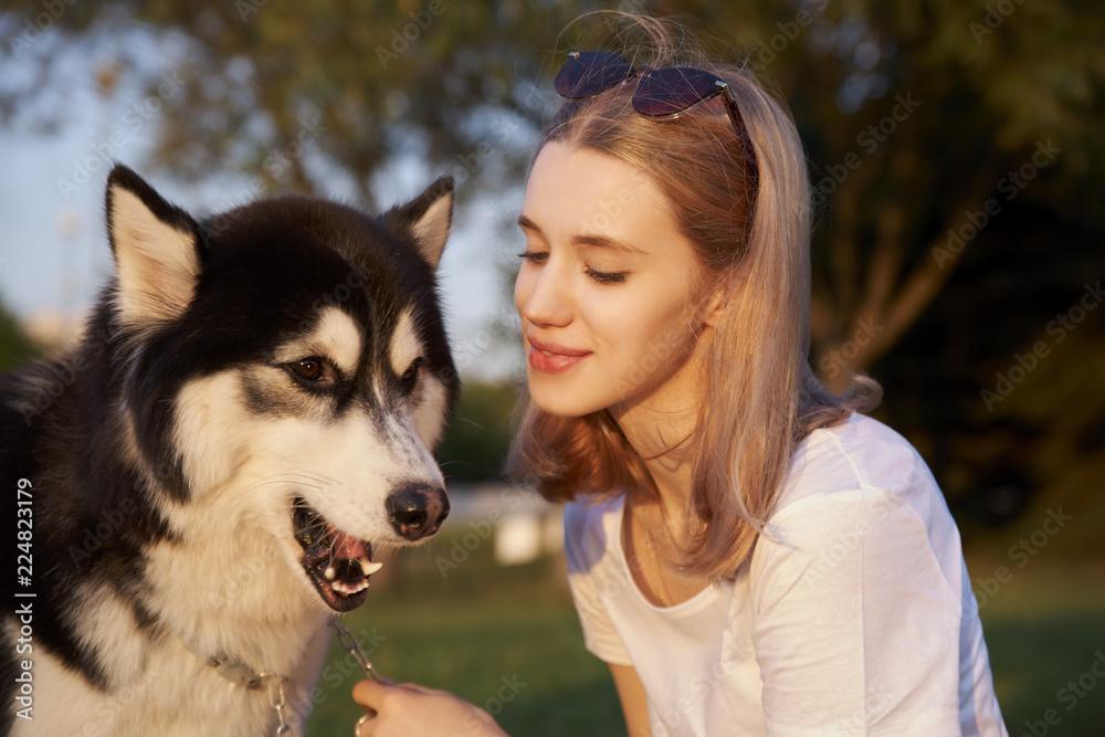 Young beautiful girl treats her pet dog Laika and smiles.Portrait on the background of greenery and trees. Young beautiful girl treats her pet dog Laika and smiles.Portrait on the background of greenery and trees.