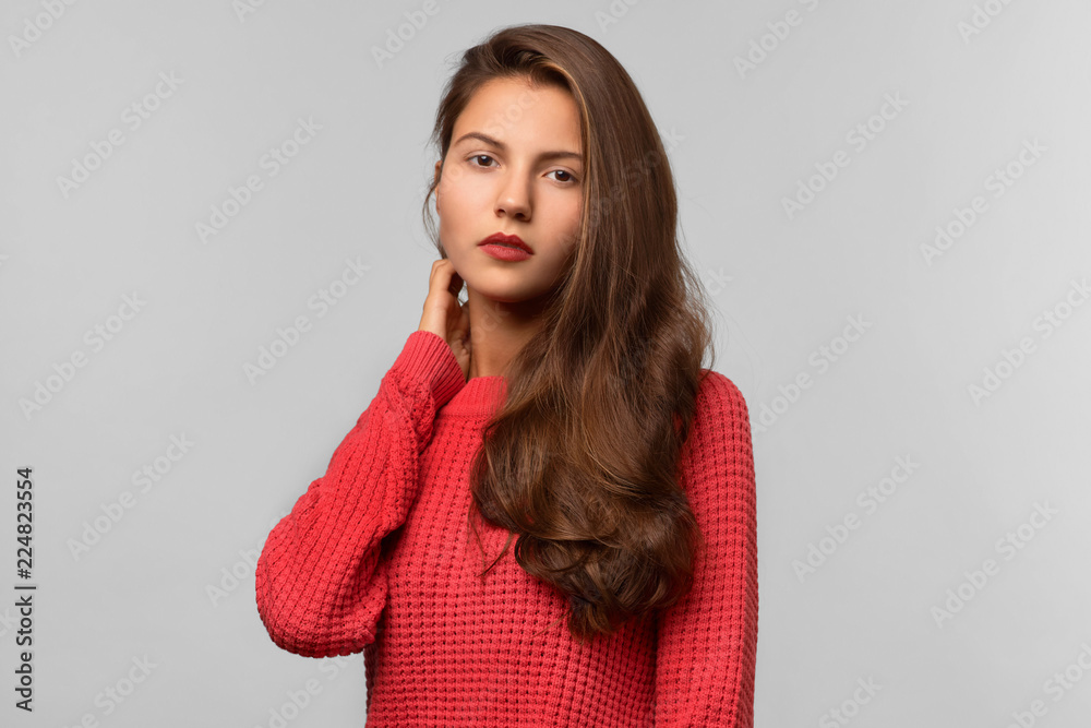 Large Studio portrait of a young beautiful girl in a red knitted sweater with long dark hair. Calm neutral expression, attentive gaze