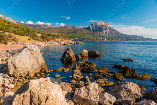 Sea shore with large boulders in the water, view of the mountain and the sea