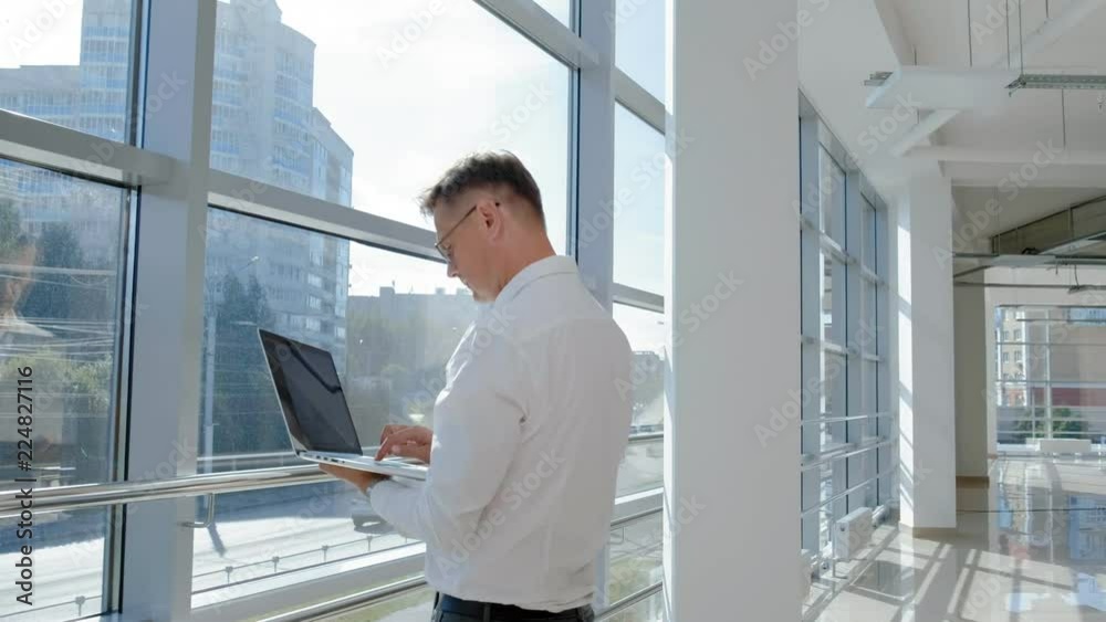 Mature businessman at a window with a laptop Mature businessman at a window with a laptop