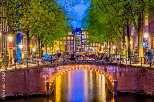 Amsterdam canal with typical dutch houses and bridge during twilight blue hour in Holland, Netherlands