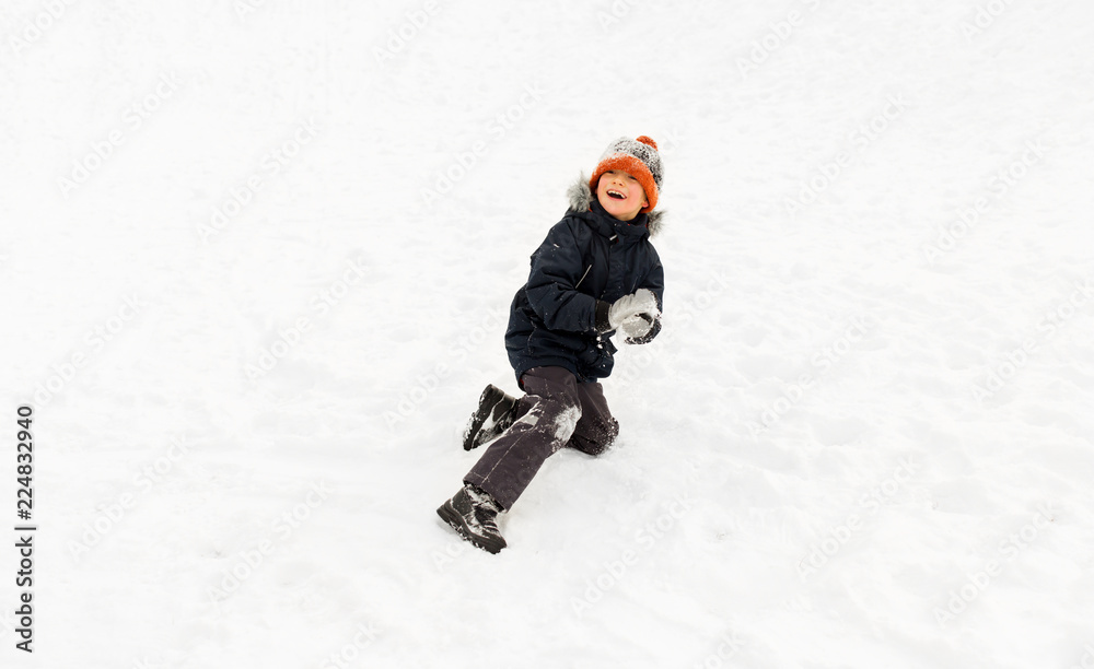 childhood, leisure and season concept - happy little boy playing with snow in winter