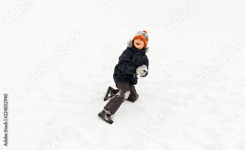 childhood, leisure and season concept - happy little boy playing with snow in winter