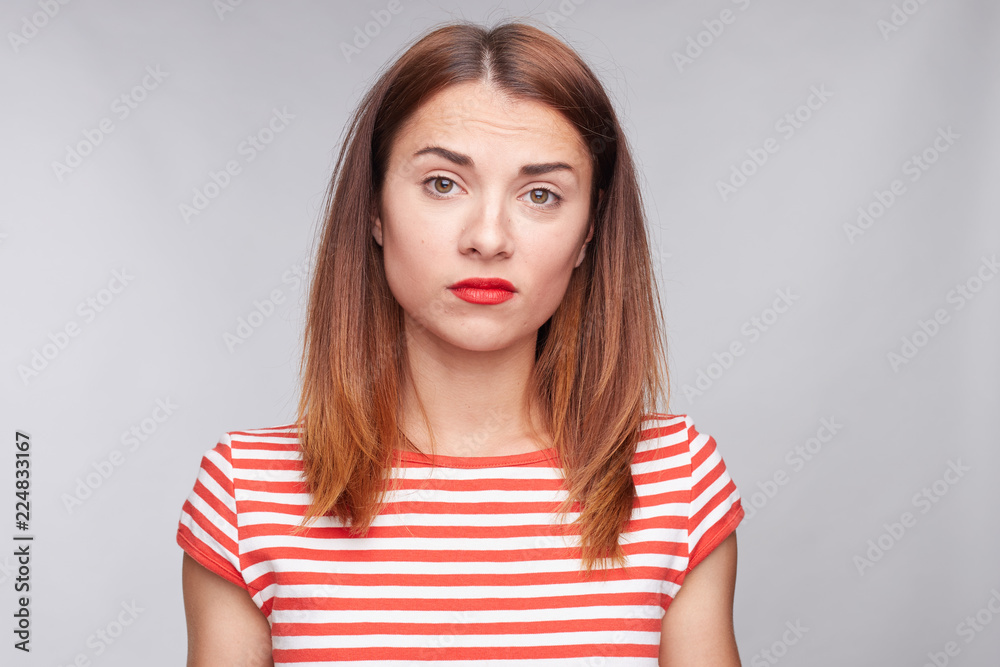 Displeased cute Caucasian female clenches teeth and shrugs shoulders with annoyance, looks at camera confusedly, dressed casually, not understanding how to solve problem. People and attitude concept. Displeased cute Caucasian female clenches teeth and shrugs shoulders with annoyance, looks at camera confusedly, dressed casually, not understanding how to solve problem. People and attitude concept.