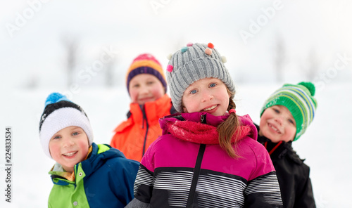 childhood, friendship and season concept - group of happy little kids in winter clothes outdoors