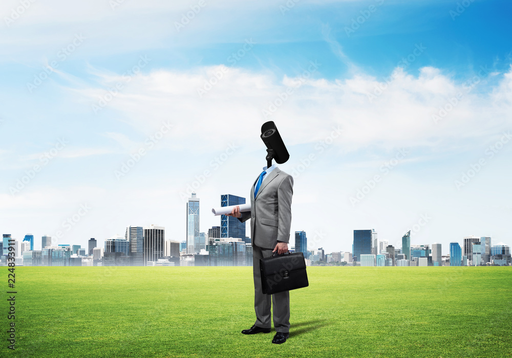 Camera headed man standing on green grass against modern cityscape Camera headed man standing on green grass against modern cityscape