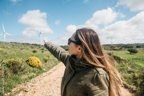 A tourist next to windmills in Portugal. She points her hand to the distance. photo