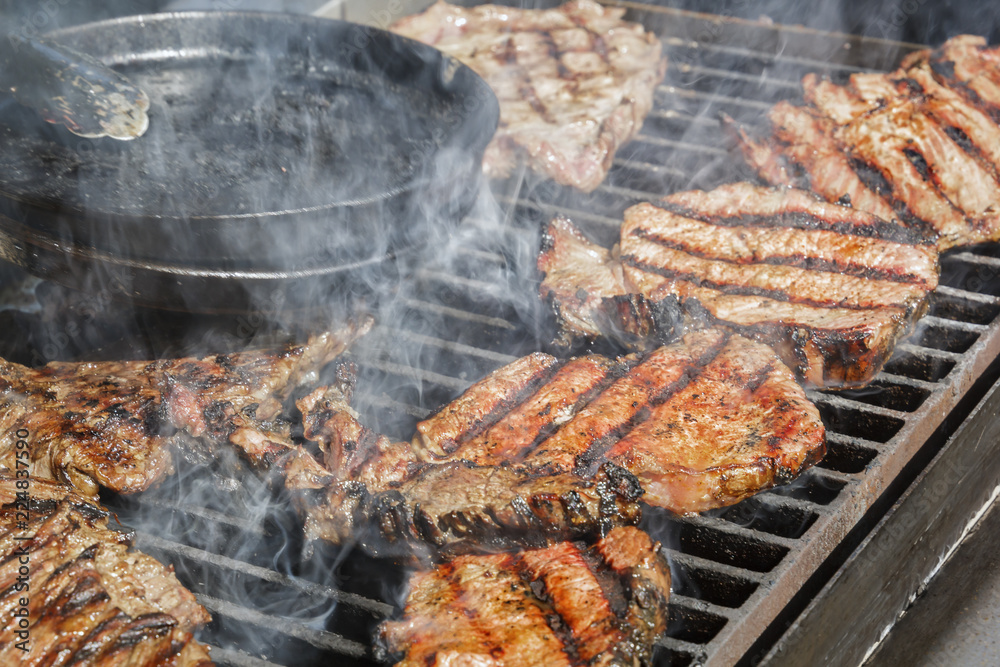 Meat steaks are cooked on a hot grill with smoke. Close-up