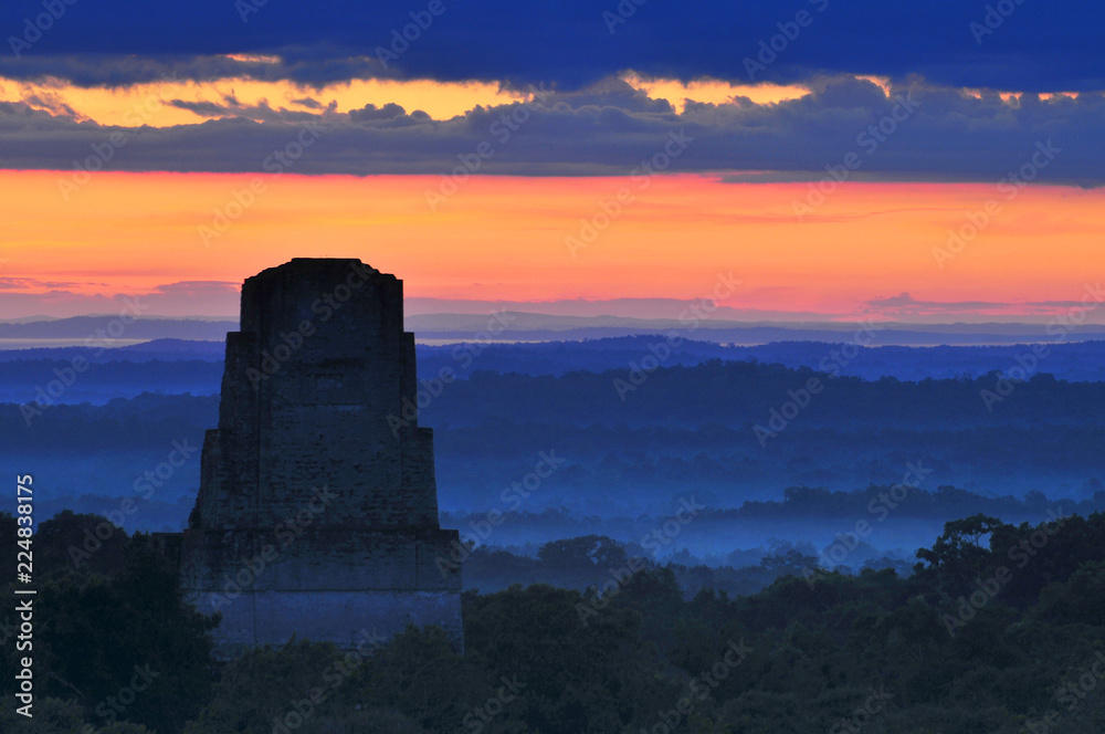 View of a sunrise above the Peten jungle with the pyramids of Tikal towering above the tree canopy in Guatemala.