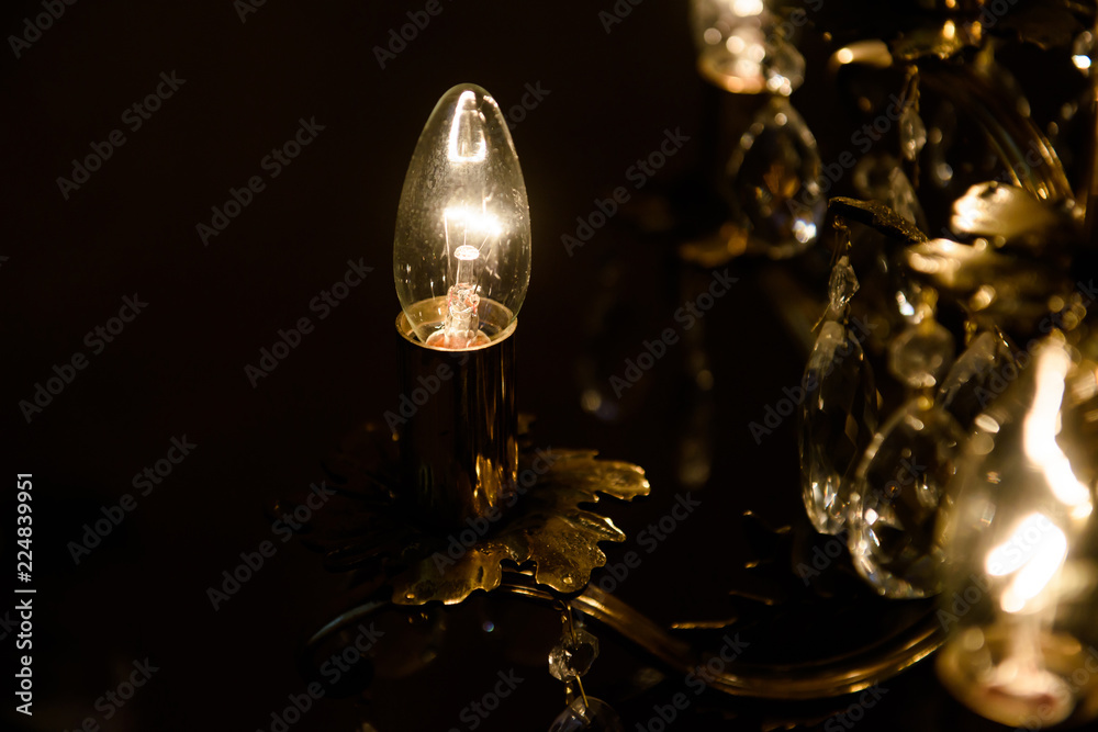 Light of the candle lit in a dark room. Vintage electric lighting in the room. 