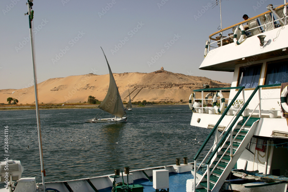 Fototapeta premium The Nile scene with feluka sail and typical landscape with sand dune near Aswan, Egypt. January, 2005