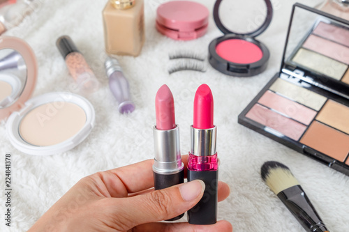 Woman hand holding two pink lipstick. Beauty cosmetic products and Various Make up accessories on the white fur background with copy space for your text. Concept of Beauty Knolling.