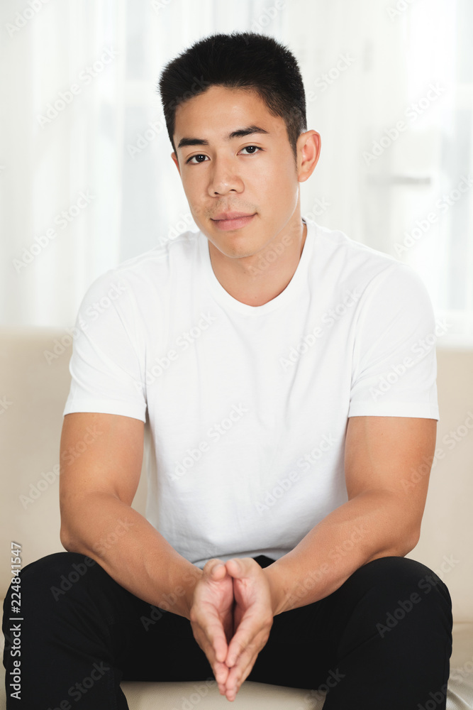 Attractive unsmiling mixed-race man sitting on couch and looking at camera Attractive unsmiling mixed-race man sitting on couch and looking at camera