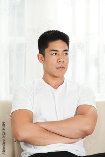 Resentful young man sitting on couch with his arms folded