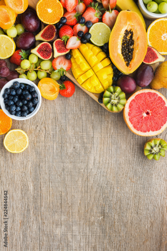 Top view of assorted fruits, strawberries blueberries, mango orange, grapefruit, banana papaya apple, grapes, kiwis on the grey wood background, copy space for text, vertical, selective focus