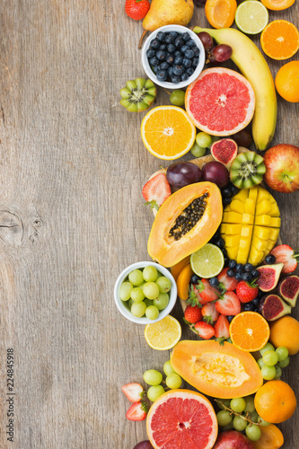 Top view of rainbow colored fruits  strawberries blueberries  mango orange  grapefruit  banana papaya apple  grapes  kiwis on the grey wood background  copy space for text  selective focus