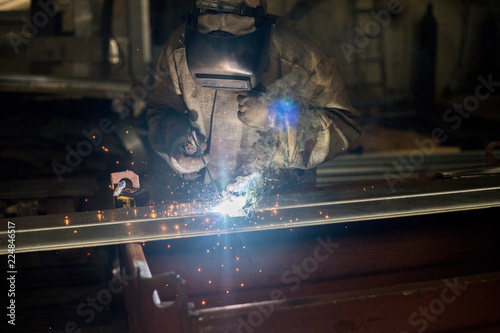 Worker in a special suit and mask performs welding work at an industrial factory
