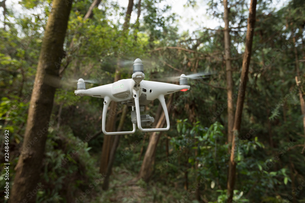 White drone with camera flying over forest