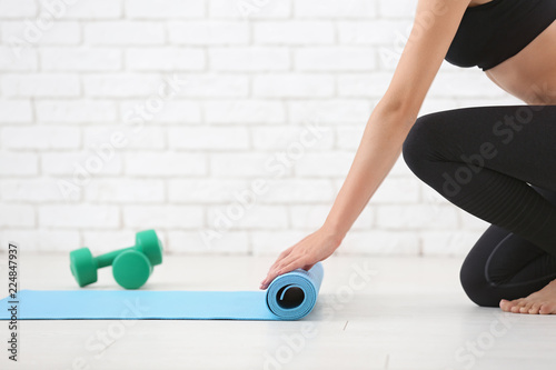 Fototapeta Naklejka Na Ścianę i Meble -  Young woman rolling yoga mat indoors