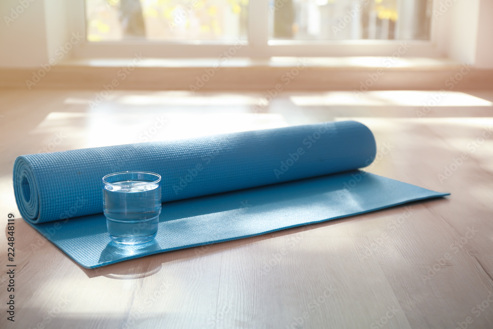 Yoga mat and glass of water on floor indoors - obrazy, fototapety, plakaty 